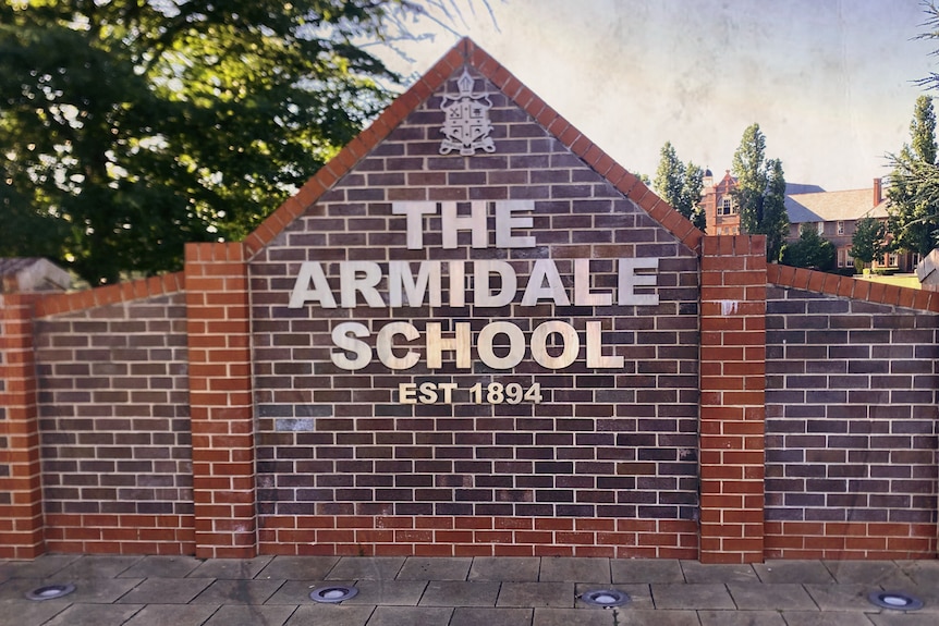 The words The Armidale School est 1894 in metal lettering and a school crest displayed on a brick wall.