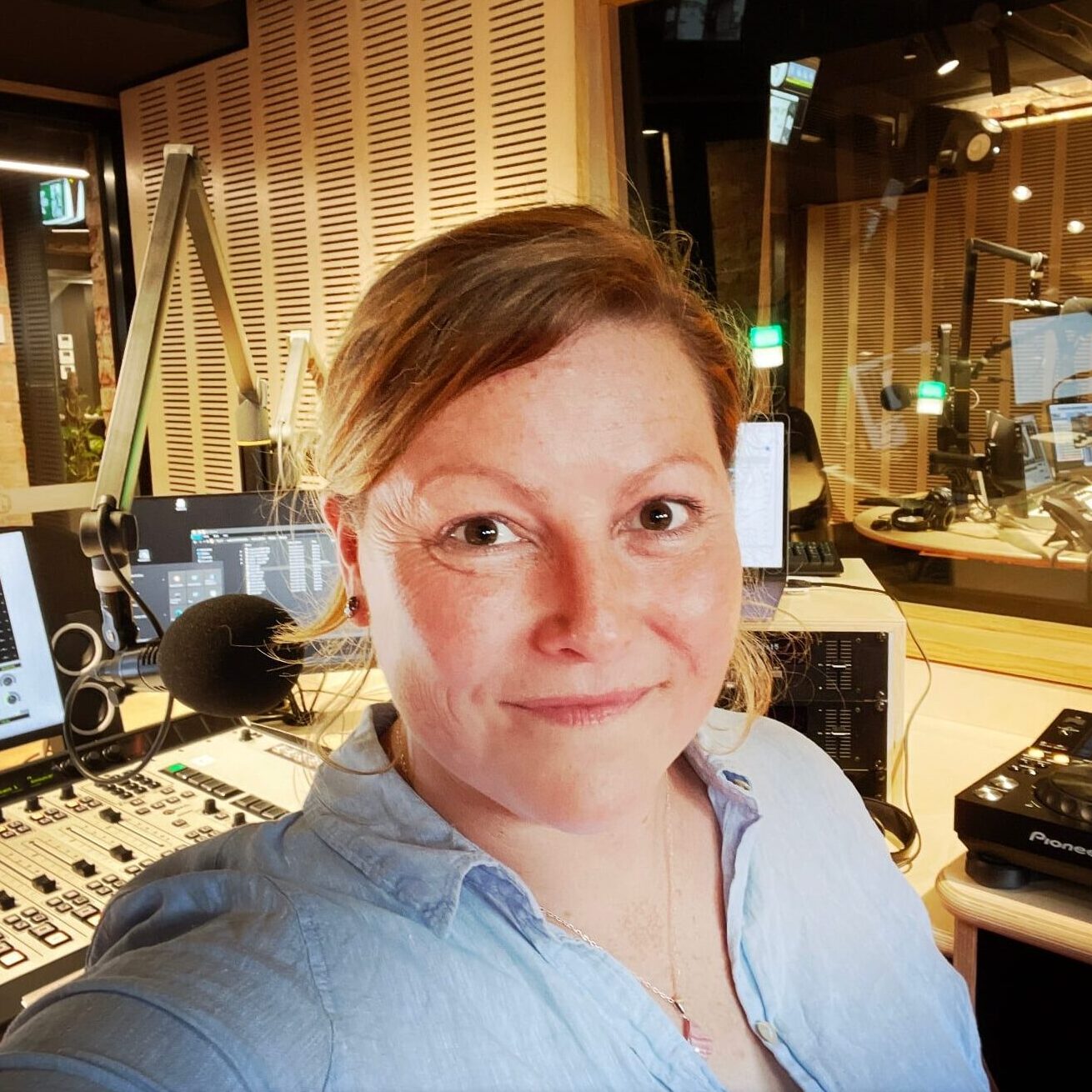Uma mulher ruiva tirando uma selfie em um estúdio de rádio.
