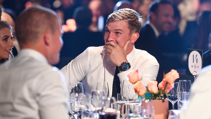 An AFL player sits with his jacket off and his hand over his mouth as he takes in the count at the Brownlow medal. 