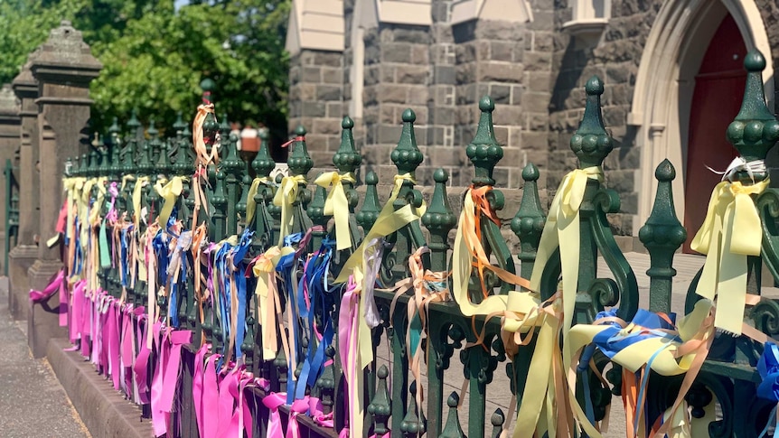 A close up of hundreds of colourful ribbons tied to a fence outside a church
