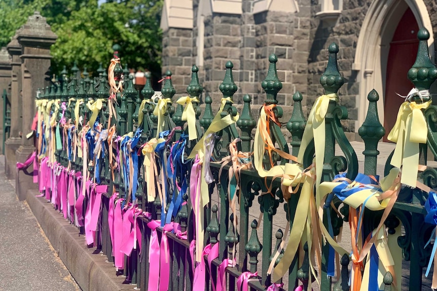 A close up of hundreds of colourful ribbons tied to a fence outside a church