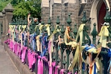 A close up of hundreds of colourful ribbons tied to a fence outside a church