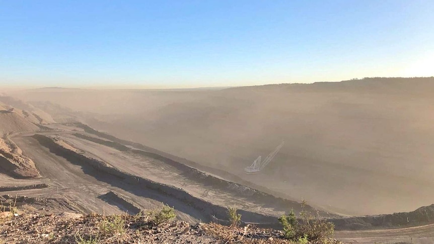 Machinery working in a dusty, open-cut coal mine.