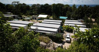 Several small one-storey buildings set in the middle of a lush, green trees with the ocean on the horizon.