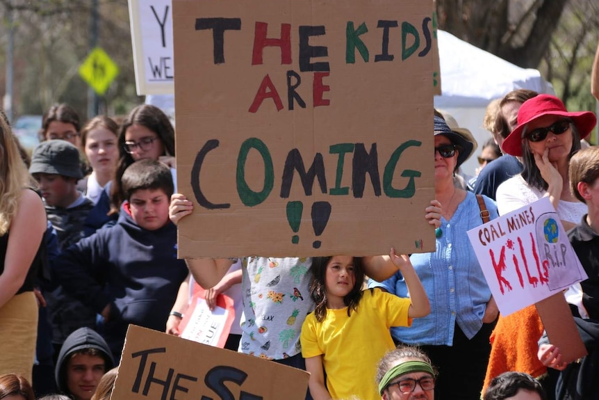 A child holding a big sign that says "the kids are coming !!"