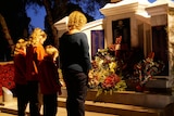 A woman and three girls in front on a war memorial and floral tributes in the pre-dawn light.