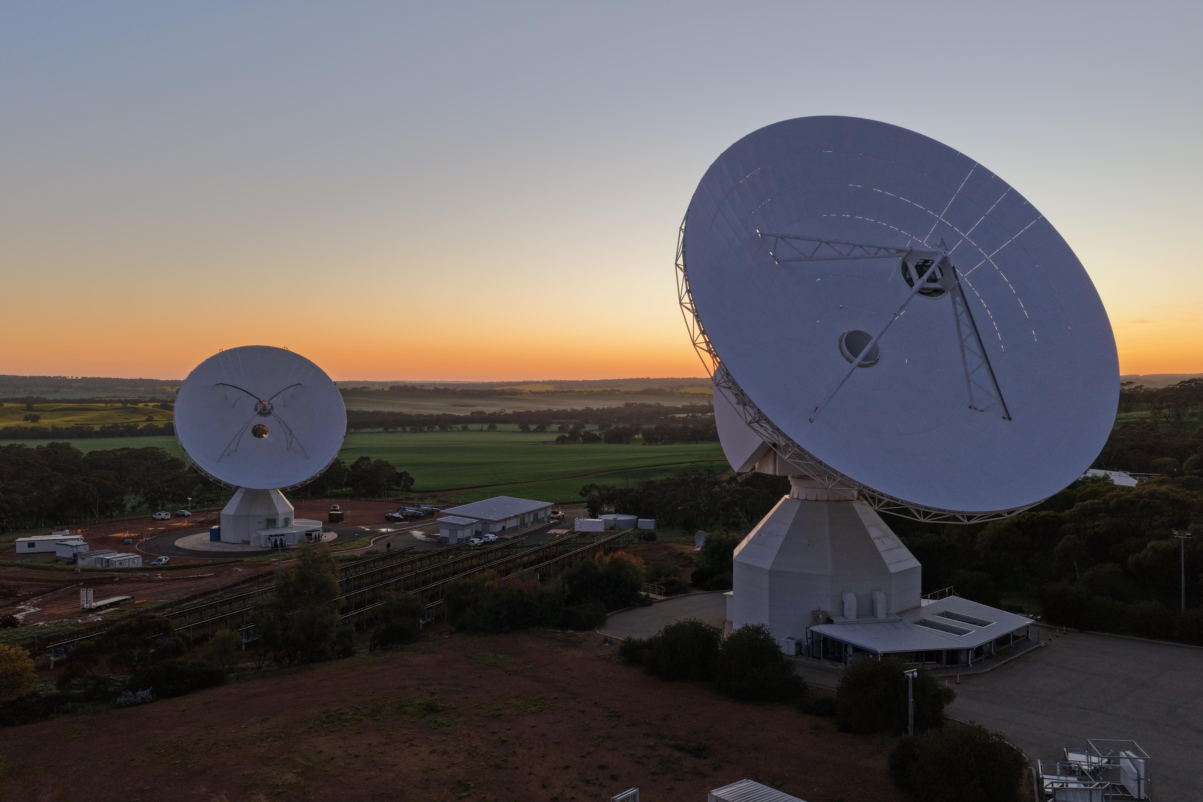 Two large space antennas surrounded by trees and red dirt in New Norcia.