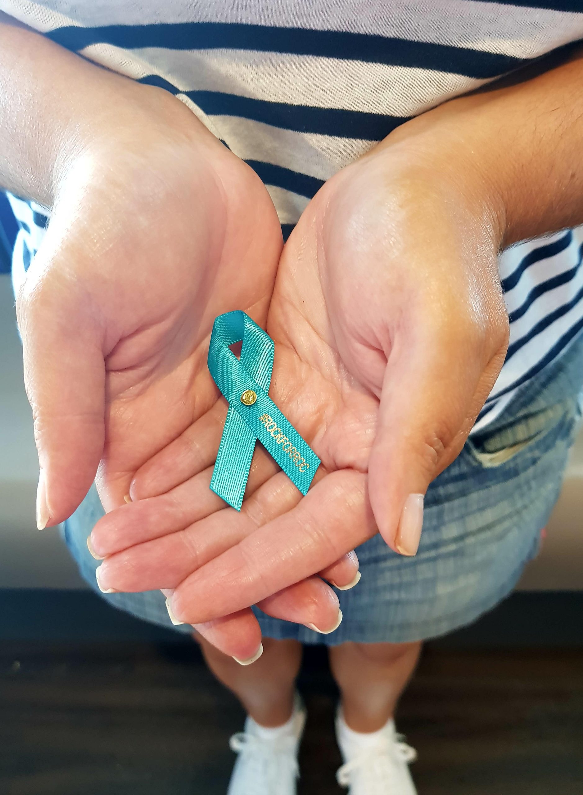 A woman holds a teal ribbon, symbolizing support for those diagnosed with ovarian cancer, in her hands.