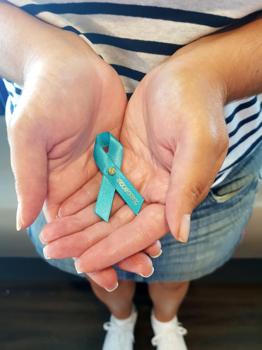 A woman holds a teal ribbon, symbolizing support for those diagnosed with ovarian cancer, in her hands.