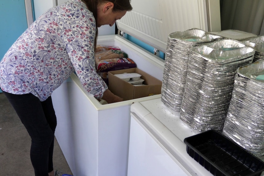 Birgit rearranges items in a deep freezer and adds meals packaged foil containers.