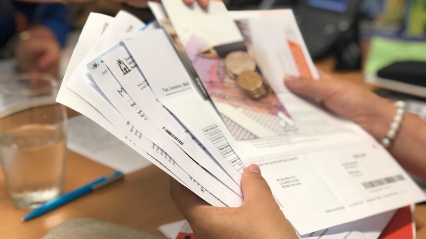 A close-up shot of a pile of unpaid bills in a person's hands with another person leaning over with a pamphlet.