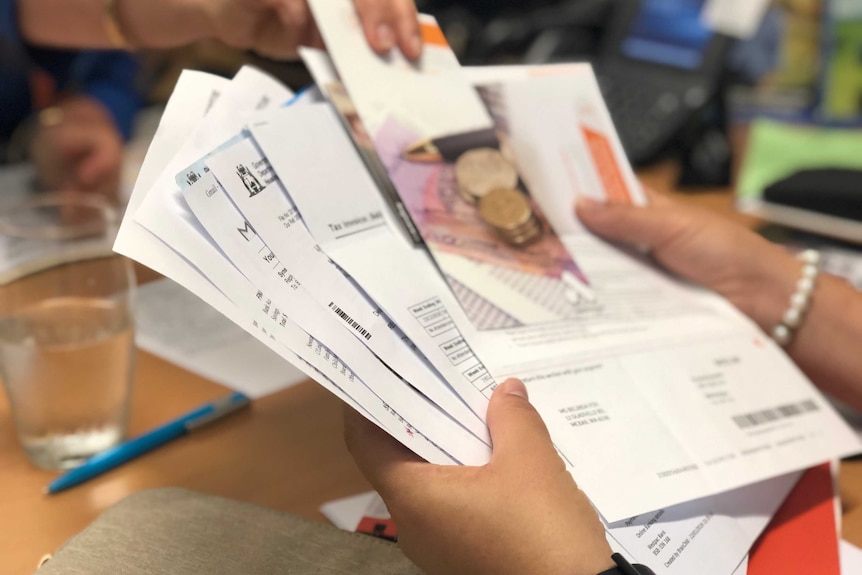 A close-up shot of a pile of unpaid bills in a person's hands with another person leaning over with a pamphlet.