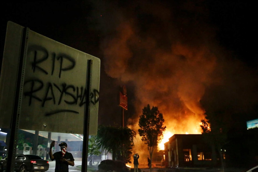 rip rayshard spray painted on a street sign as fire rises behind