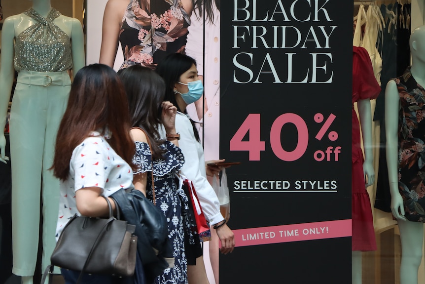 Three women walk past a Black Friday sale sign in a shop window.