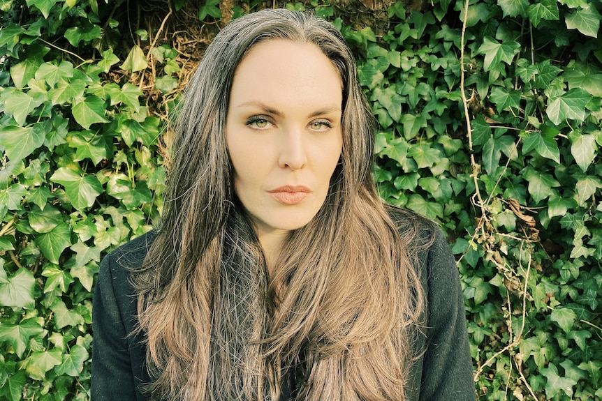 A women wearing black, standing in front of a hedge