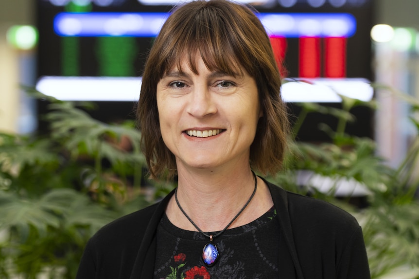 A woman wearing a red and black flowery top looks towards the camera.