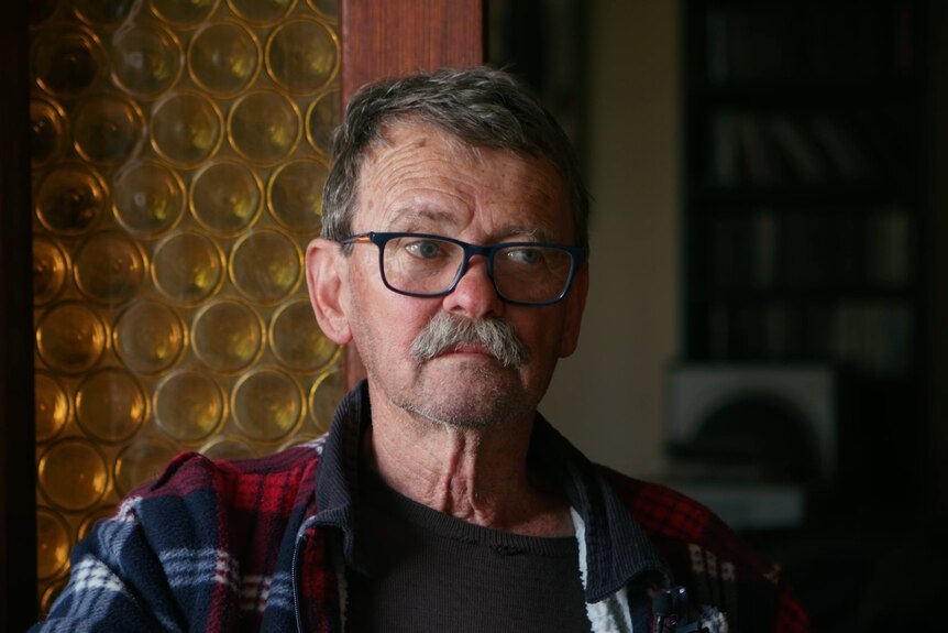 a portrait of a man in his 70s, he has glasses and is wearing a flannalette shirt