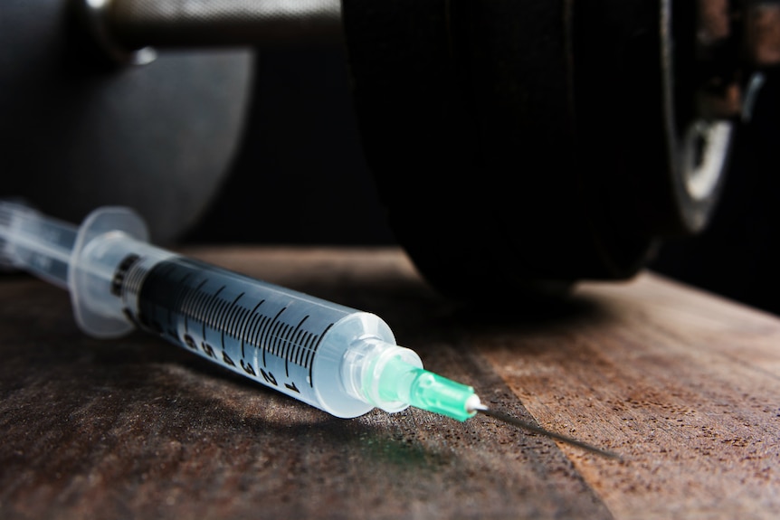 A syringe filled with steroids next to a gym dumb bell.