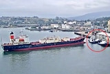 A large ship about to directly hit two small tugboats.