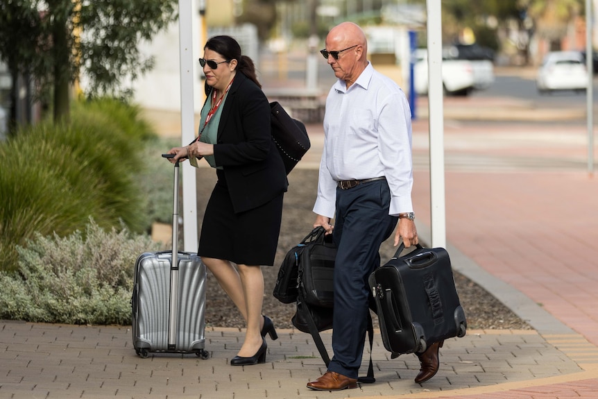 A man and a woman with briefcases walking into a police station.  