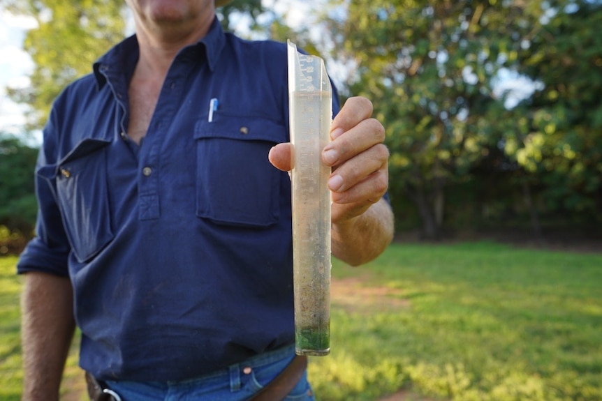 Man holding full rain gauge in his outstretched hand.