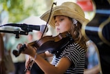 A young girl in a straw hat plays the fiddle on Peel Street