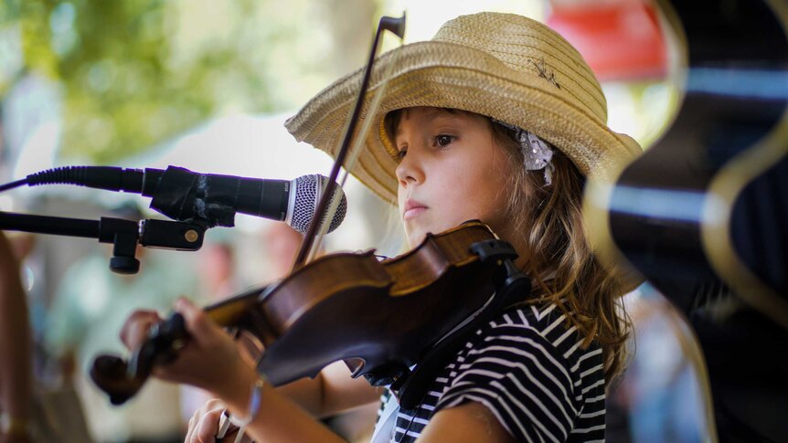 A young girl in a straw hat plays the fiddle on Peel Street