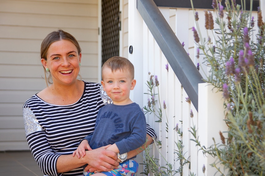 Woman sitting on front steps of home with toddler son
