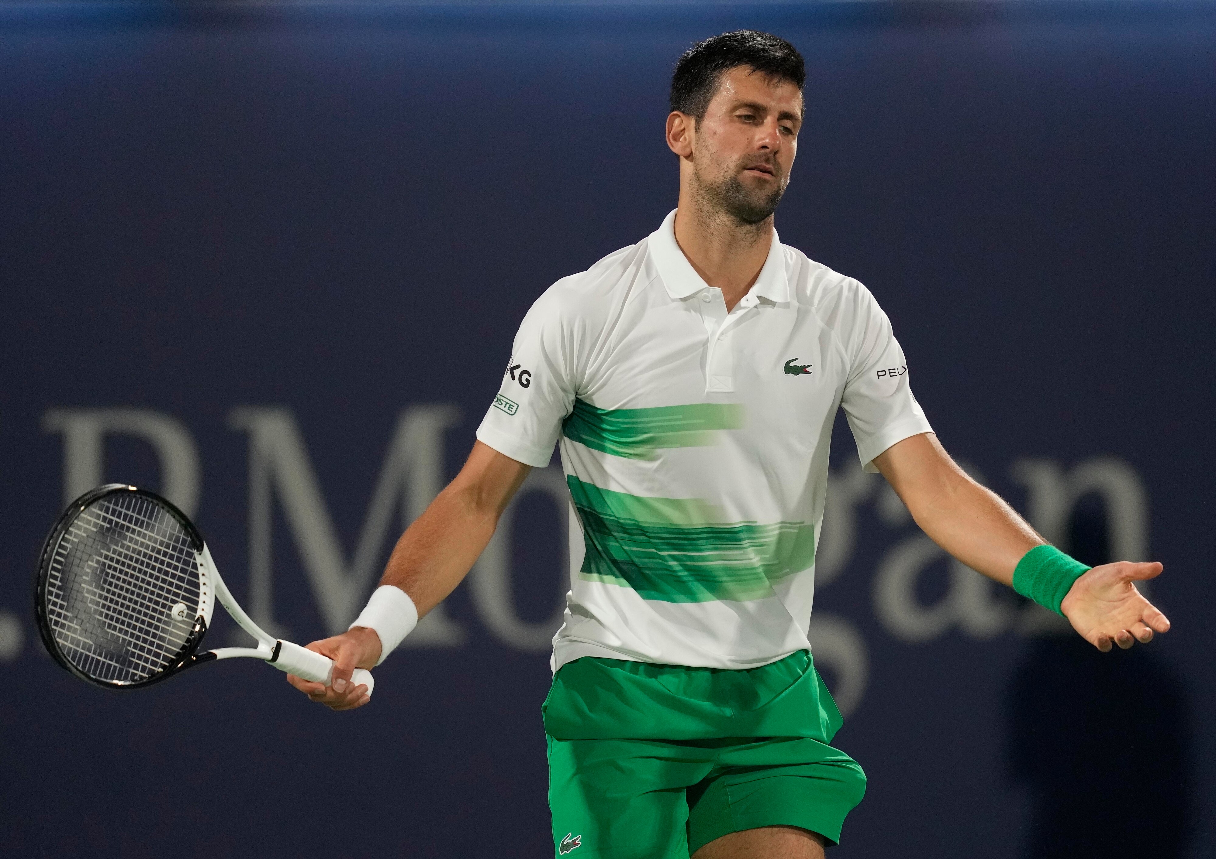 A disgruntled-looking Novak Djokovic spreads his arms wide as he looks down at the court  after a point during a match.