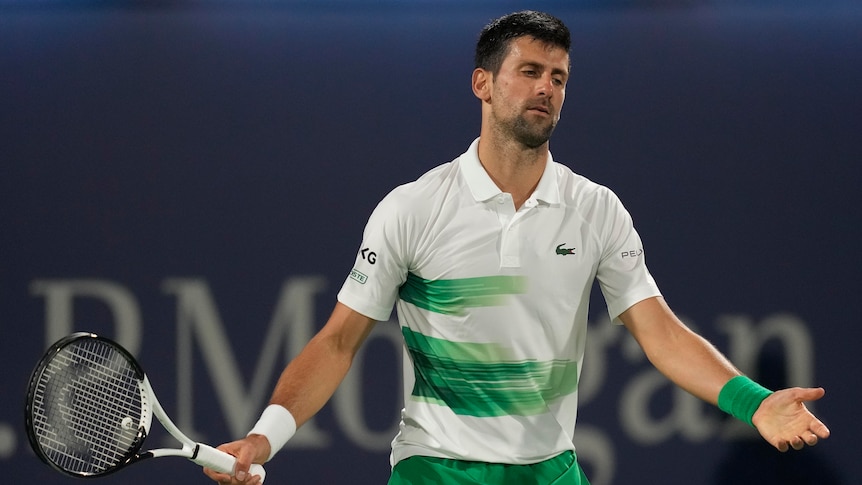 A disgruntled-looking Novak Djokovic spreads his arms wide as he looks down at the court  after a point during a match.