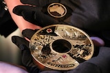 A pair of gloved hands hold the $2.48 million holed Discovery gold and Argyle pink diamond coin and its insert.
