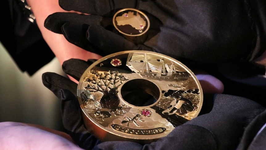 A pair of gloved hands hold the $2.48 million holed Discovery gold and Argyle pink diamond coin and its insert.