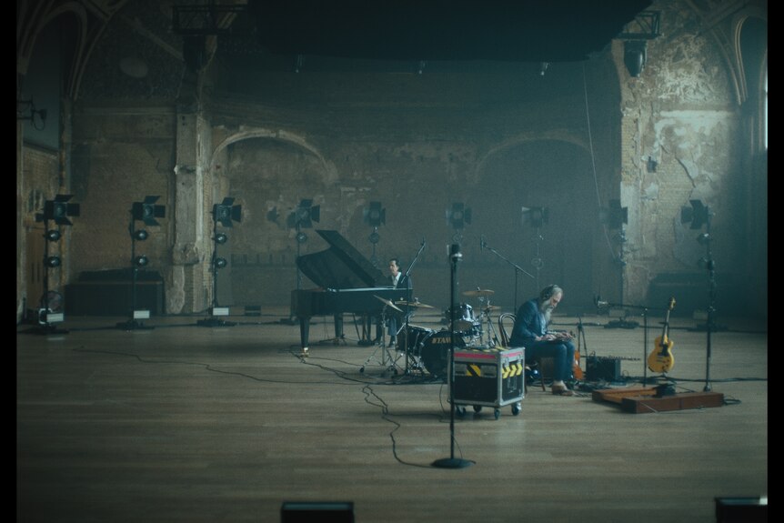 In a cavernous rehearsal space, Nick Cave sits at a grand piano, while Warren Ellis sits with a synthesiser on his lap