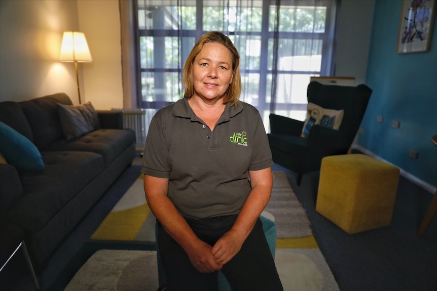 A woman in a polo shirt sits in a teen counselling space.