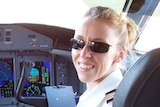 A woman smiles while sitting in the cockpit of a plane. She's wearing sunglasses
