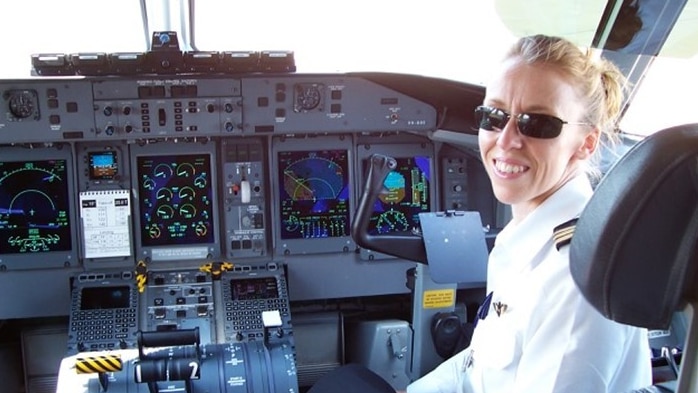 A woman smiles while sitting in the cockpit of a plane. She's wearing sunglasses
