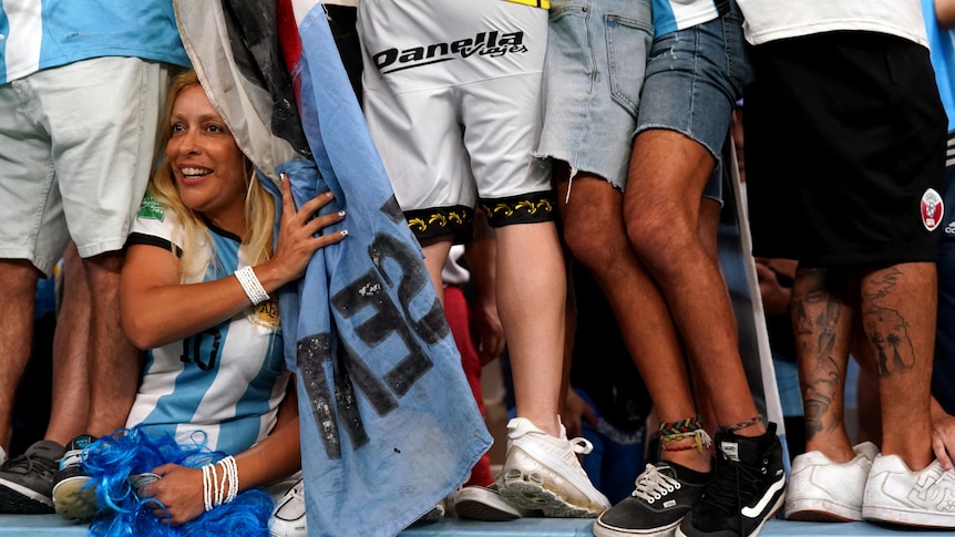 An Argentinian fan tries to get a look at the field as her fellow supporters climb the fence to chant for their team.