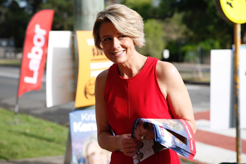 Bennelong Labor candidate Kristina Keneally wears red and stands outside a polling booth with campaign material.