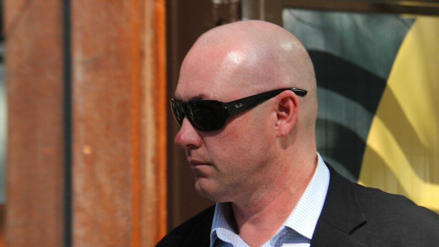 A bald man in a suit and sunglasses walks in the sunshine outside a building in Perth's CBD.