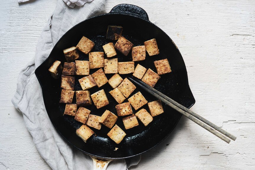 A cast iron skillet filled with pan fried cubes of tofu, a key ingredient for a vegetarian salad for dinner.