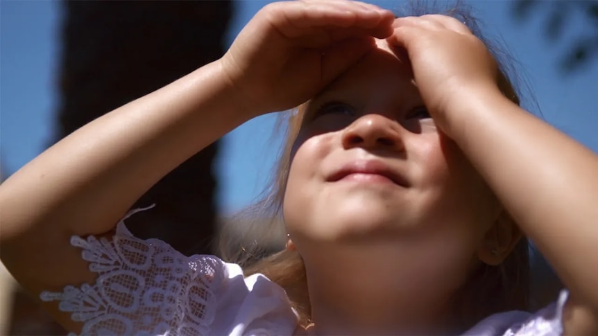 A girl shielding her eyes looking up at the sky
