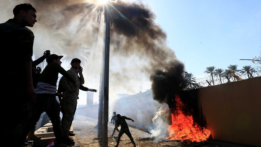 Protesters set fire outside the wall of the US embassy in Bagdad, with smoke rising into the sky.