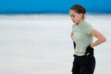 Figure skater Kamila Valieva stands with her hands on her hips on the ice rink. The Olympic rings and "Beijing" are on the wall.