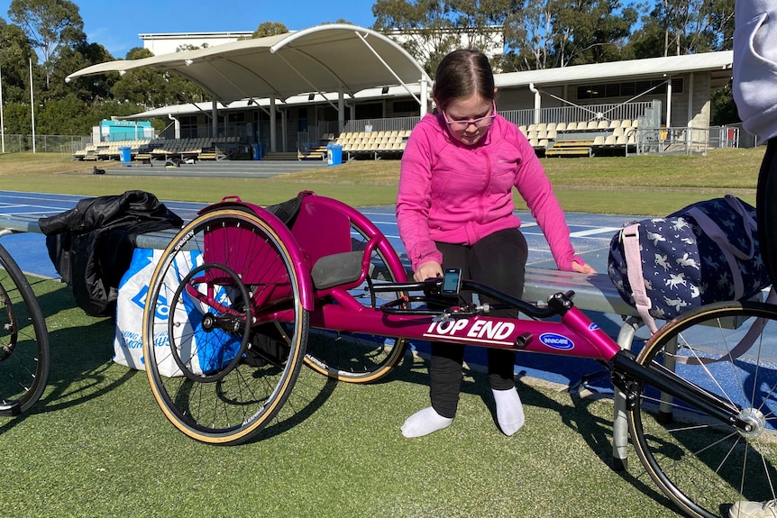 A young wheelchair athlete checks her racing chair next to a track.