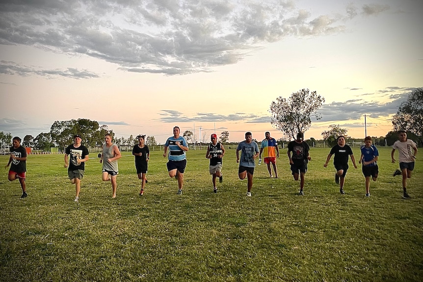 A line of young men run on a grassy field.