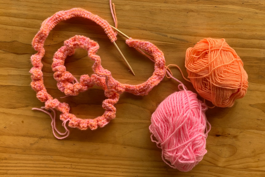 Two bundles of pink and orange yarn and the start of a knitted blanket.