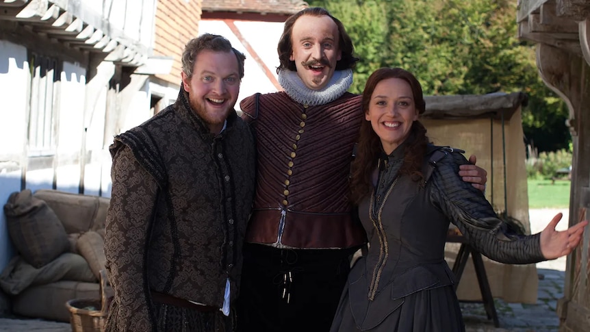 A man dressed as Shakespeare and two people in period dress a group smiling