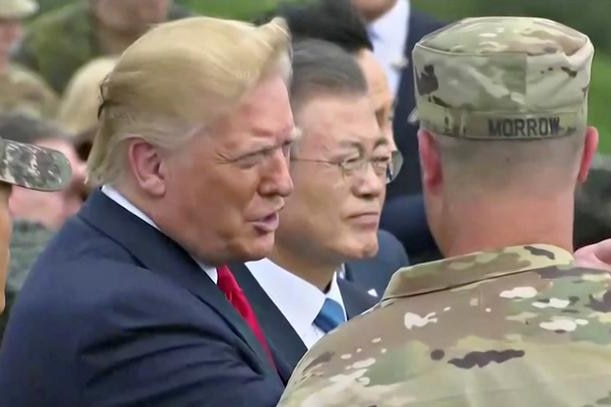 Donald Trump looks straight ahead and points as he is flanked by two soldiers with Moon Jae-in to his right.