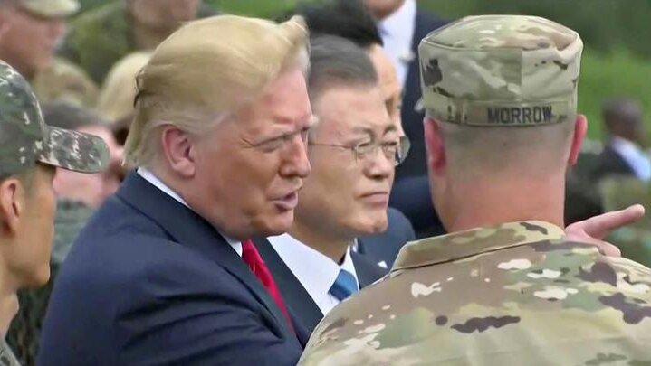 Donald Trump looks straight ahead and points as he is flanked by two soldiers with Moon Jae-in to his right.