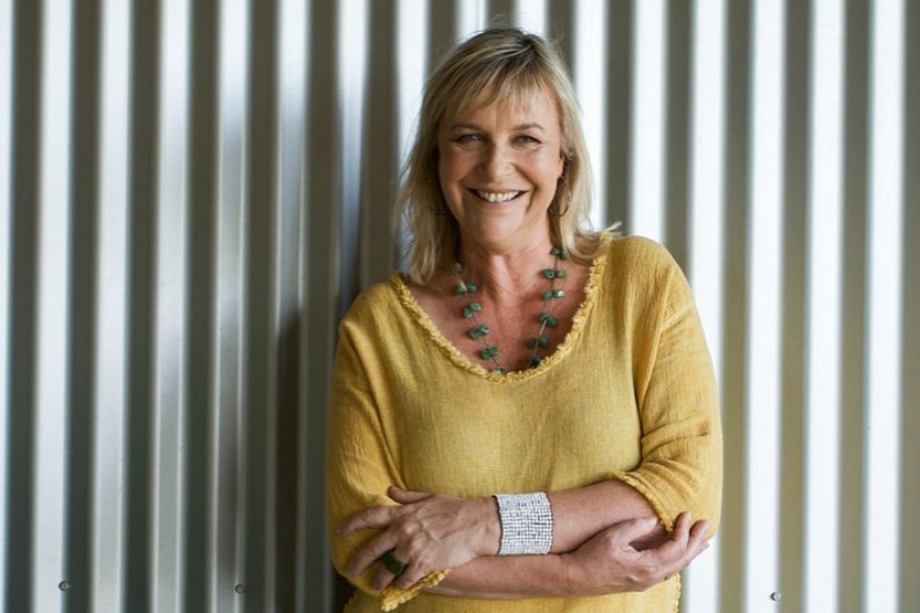 A woman wears a yellow shirt, folds her arms and smiles at the camera.